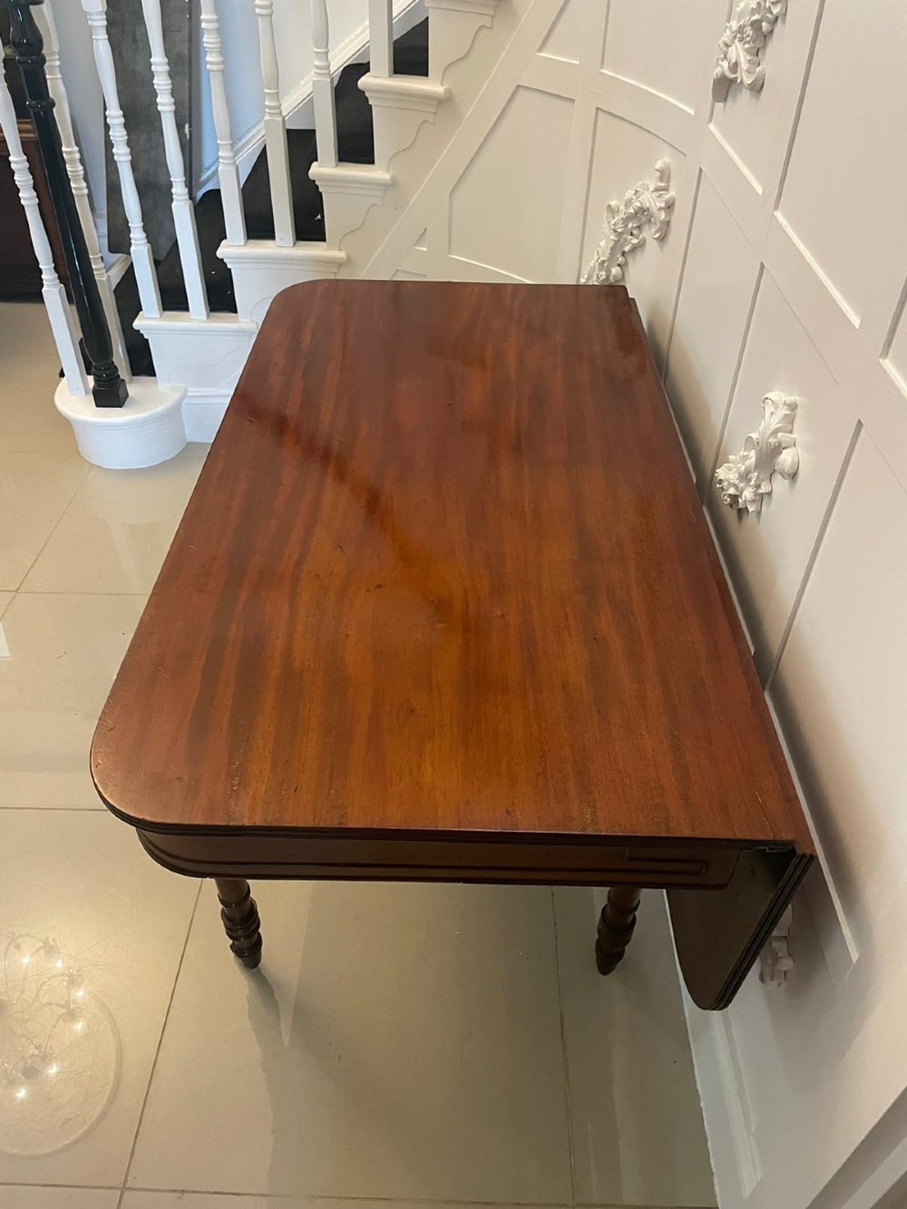 An antique George III mahogany console table featuring a polished rectangular top with rounded corners, a panelled frieze, and turned legs on brass castors. View XIII
