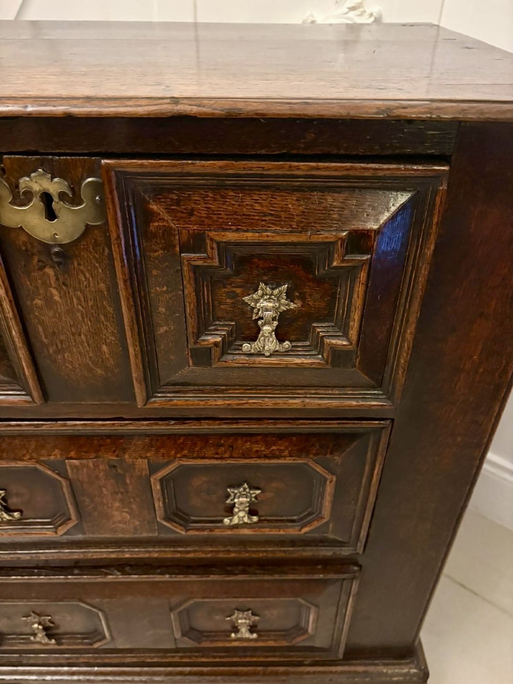 A dark oak Jacobean chest of drawers featuring geometric moulded drawer fronts and brass drop handles. View IV
