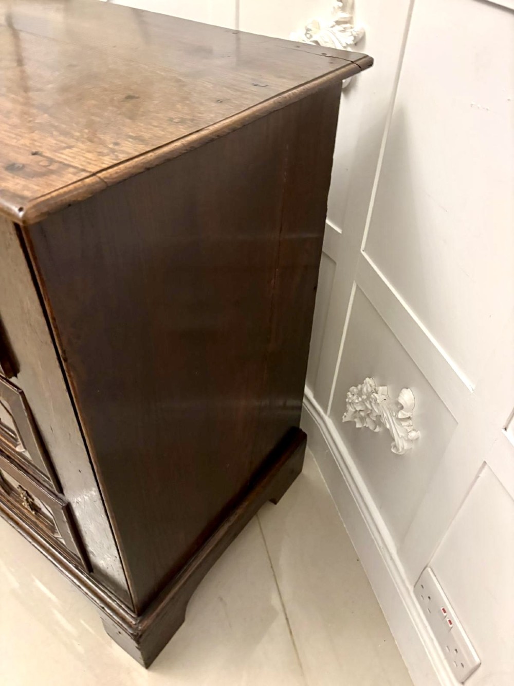 A dark oak Jacobean chest of drawers featuring geometric moulded drawer fronts and brass drop handles. View V