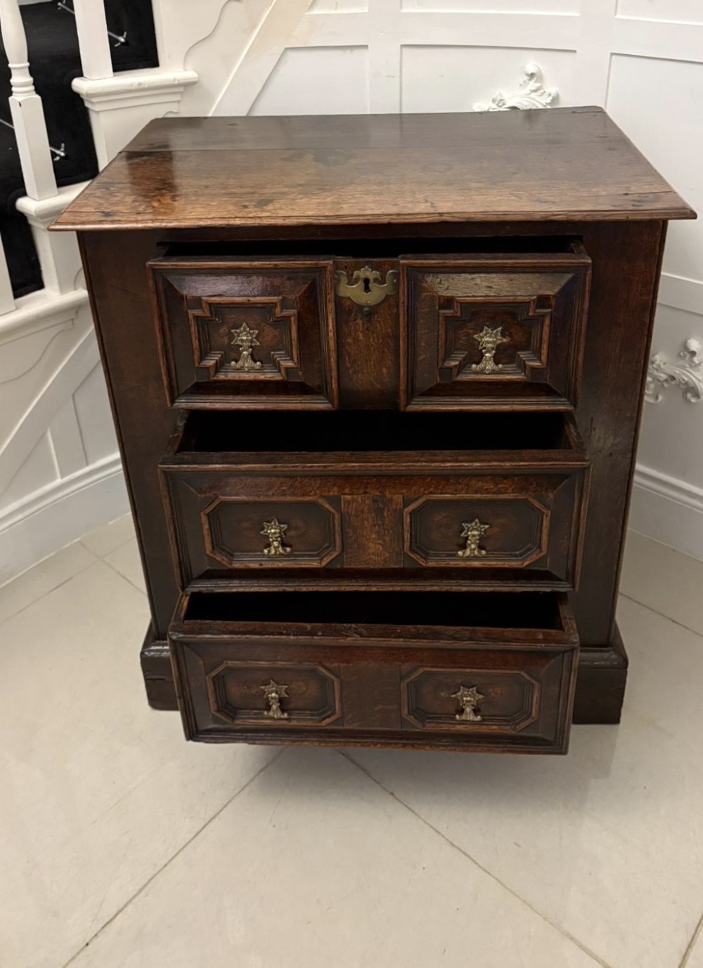 A dark oak Jacobean chest of drawers featuring geometric moulded drawer fronts and brass drop handles. View VI