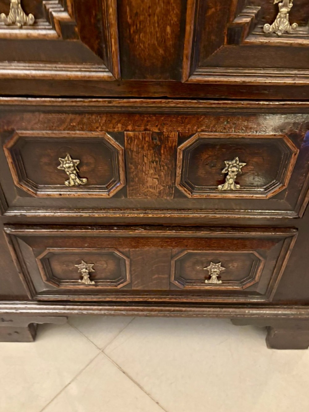 A dark oak Jacobean chest of drawers featuring geometric moulded drawer fronts and brass drop handles. View X