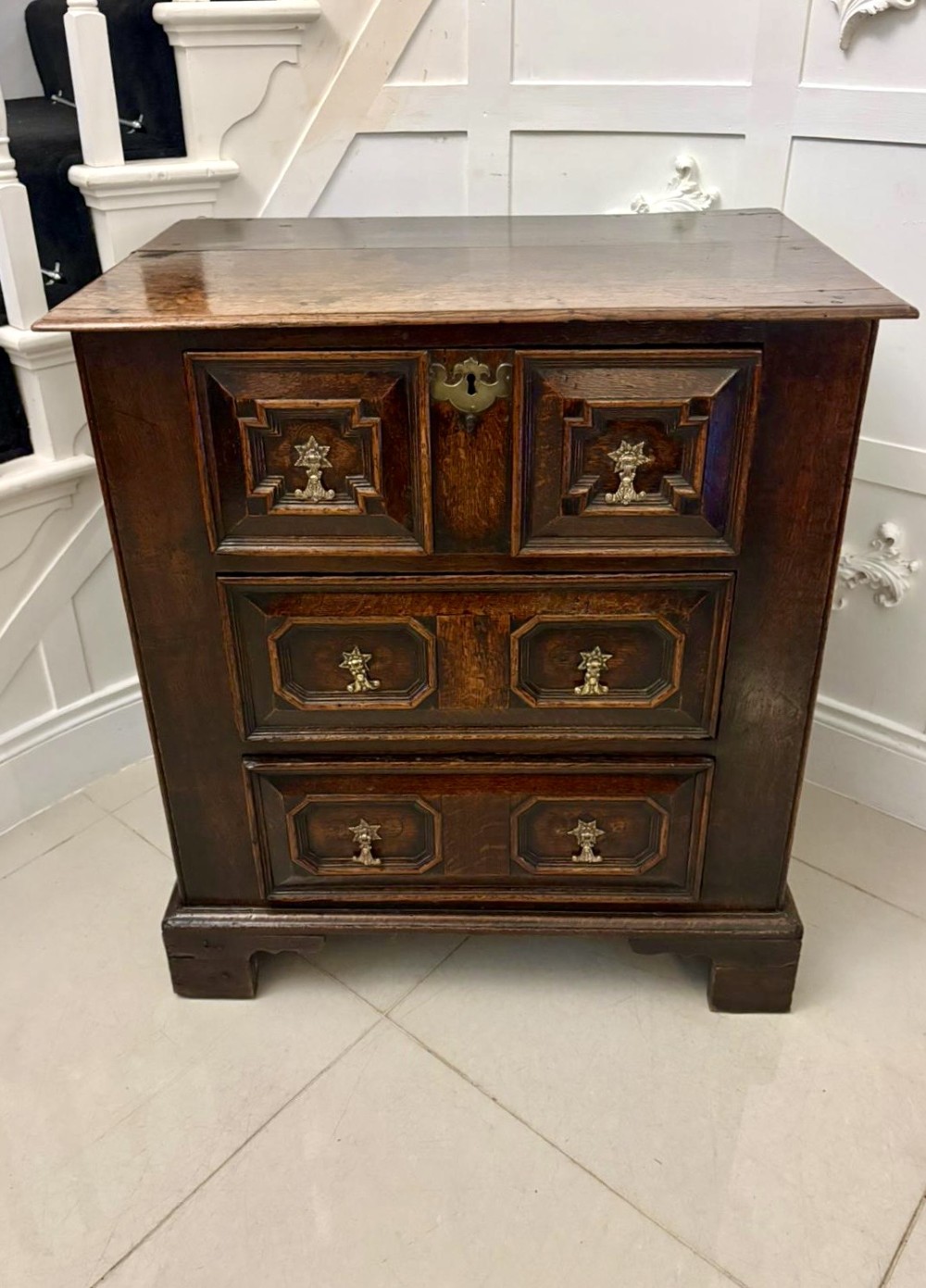 A dark oak Jacobean chest of drawers featuring geometric moulded drawer fronts and brass drop handles.