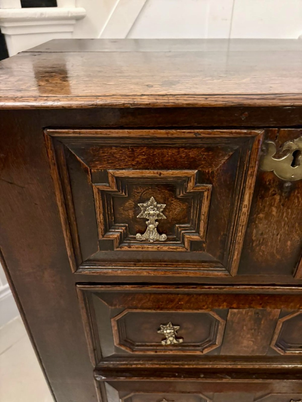 A dark oak Jacobean chest of drawers featuring geometric moulded drawer fronts and brass drop handles. View XI
