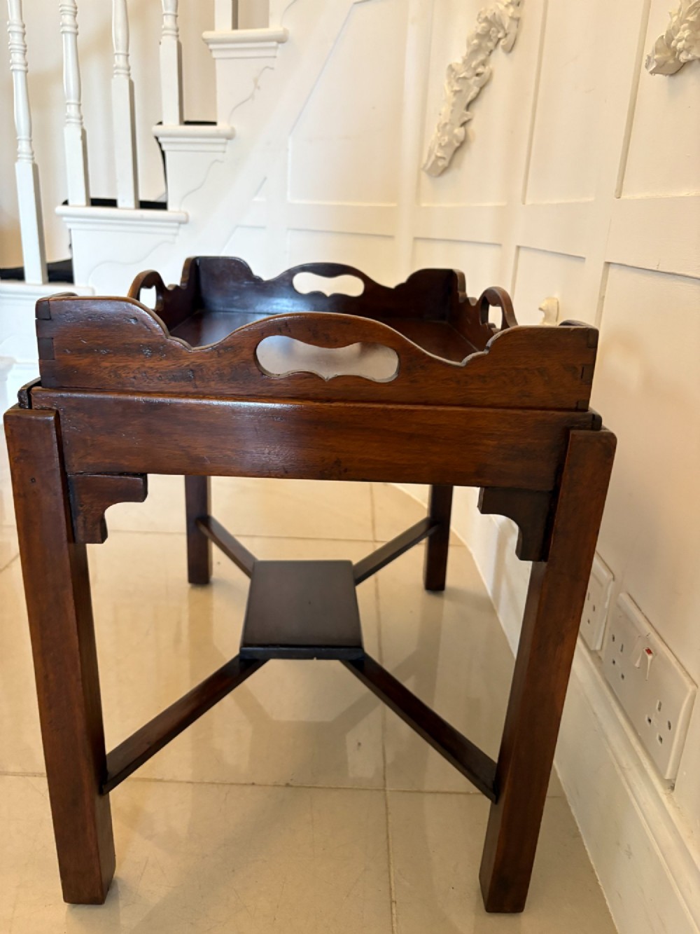 An Edwardian dark mahogany butlers tray featuring cut-out hand holes and a galleried rim, resting on a sturdy matching wooden stand with X-stretchers. View III