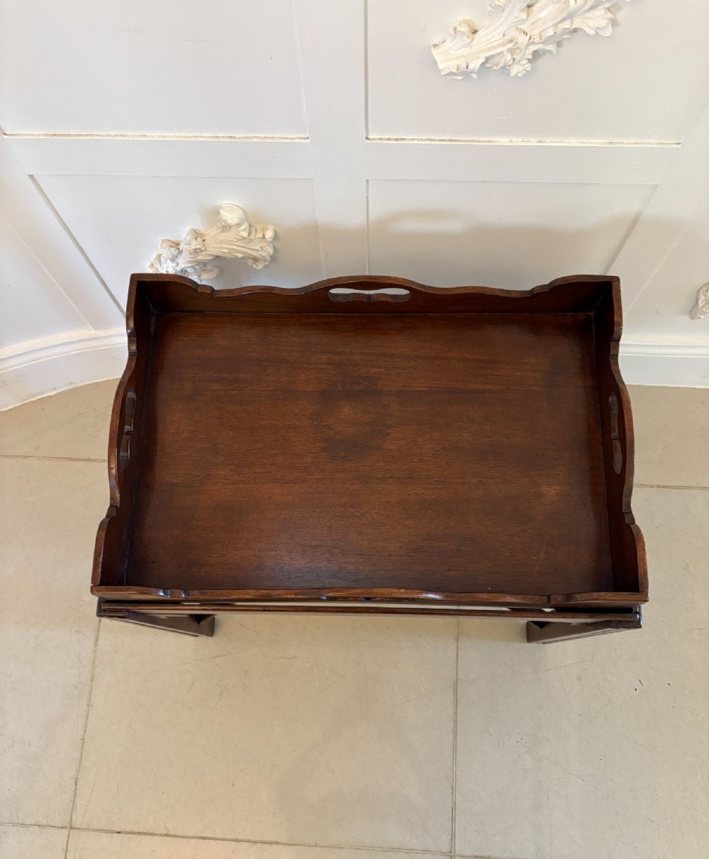 An Edwardian dark mahogany butlers tray featuring cut-out hand holes and a galleried rim, resting on a sturdy matching wooden stand with X-stretchers. View V