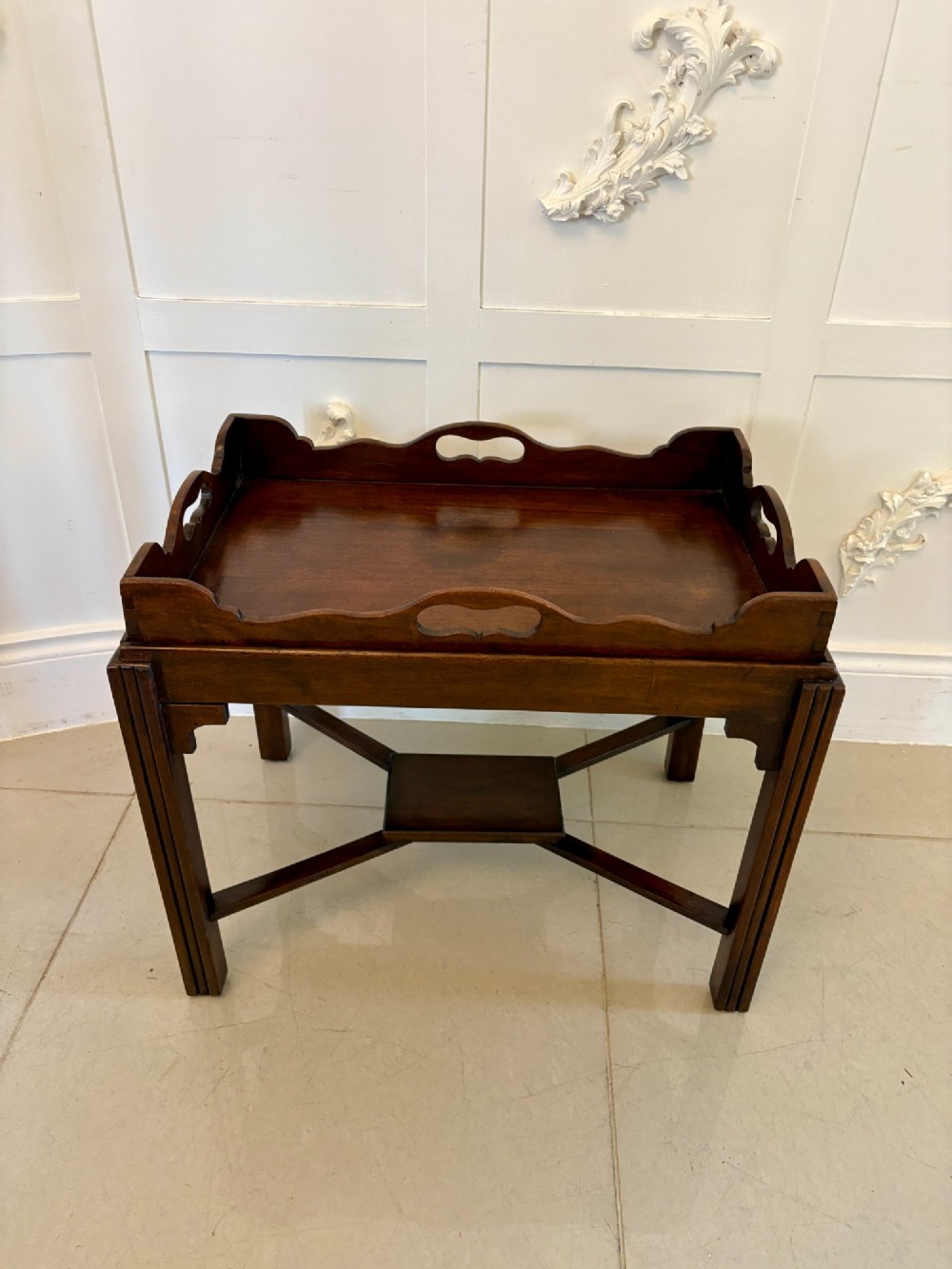 An Edwardian dark mahogany butlers tray featuring cut-out hand holes and a galleried rim, resting on a sturdy matching wooden stand with X-stretchers.