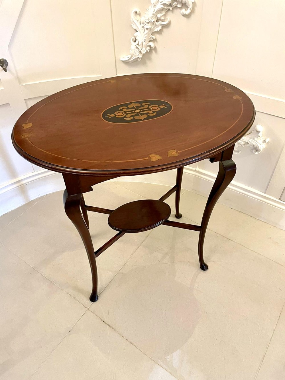 An oval mahogany lamp table featuring Art Nouveau central marquetry inlay, slender curved legs, and a lower oval shelf.