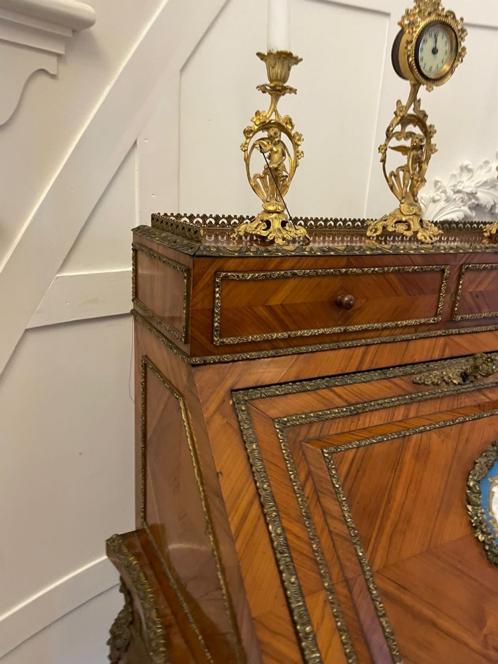 A French-style kingwood slant-front bureau featuring geometric wood parquetry, ornate gilt-bronze mounts, cabriole legs, and a central porcelain medallion. View V