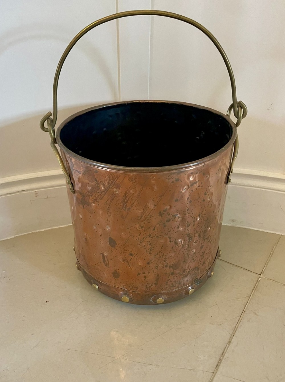 An antique copper coal bucket featuring a hand-hammered finish, brass swing handle, and a row of brass rivets around the lower rim.