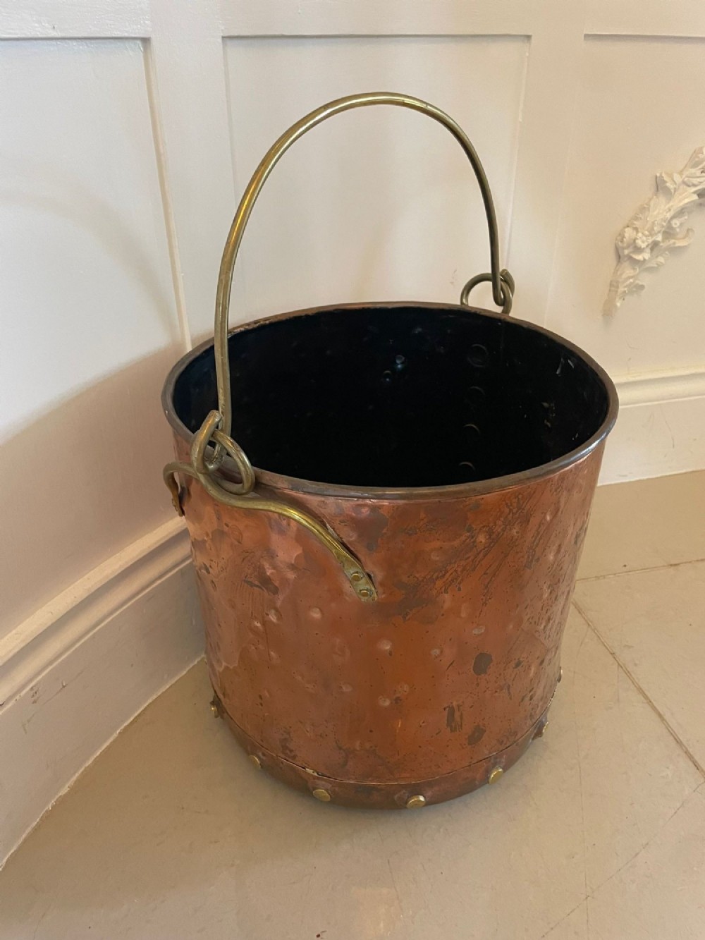 An antique copper coal bucket featuring a hand-hammered finish, brass swing handle, and a row of brass rivets around the lower rim. View V