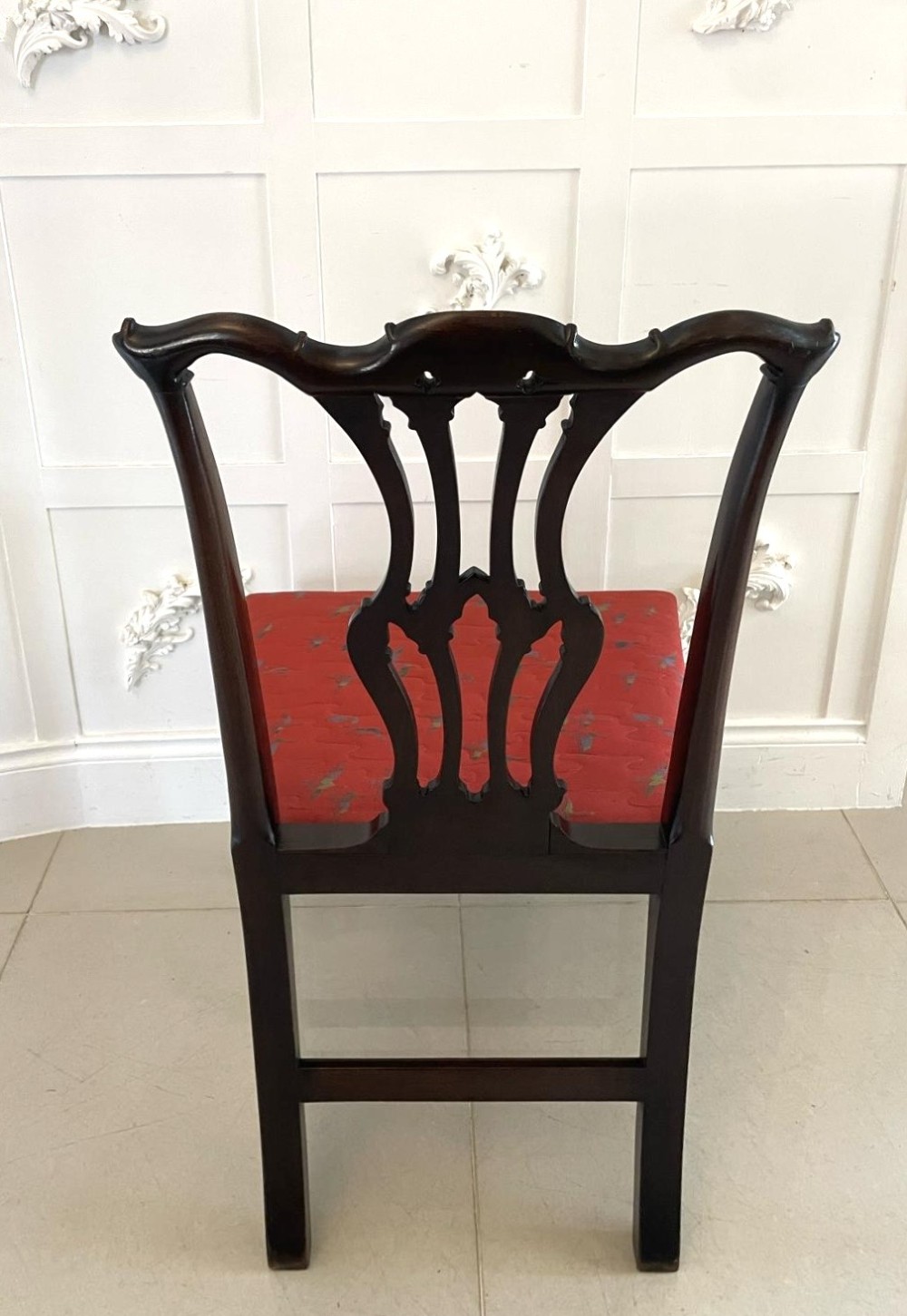 A set of twelve carved dark mahogany dining chairs featuring intricate pierced back splats and red patterned upholstered seats. View II