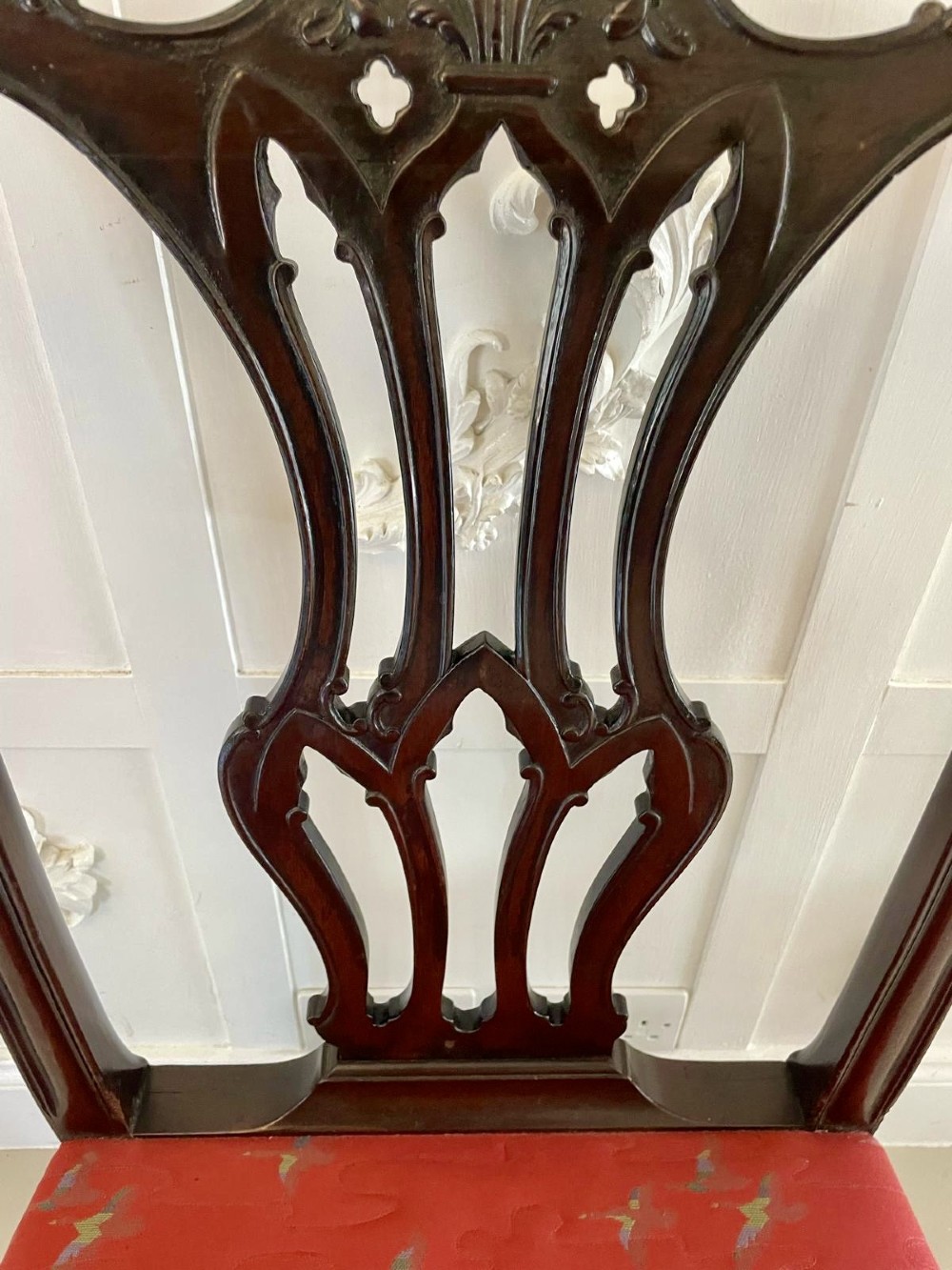 A set of twelve carved dark mahogany dining chairs featuring intricate pierced back splats and red patterned upholstered seats. View IV