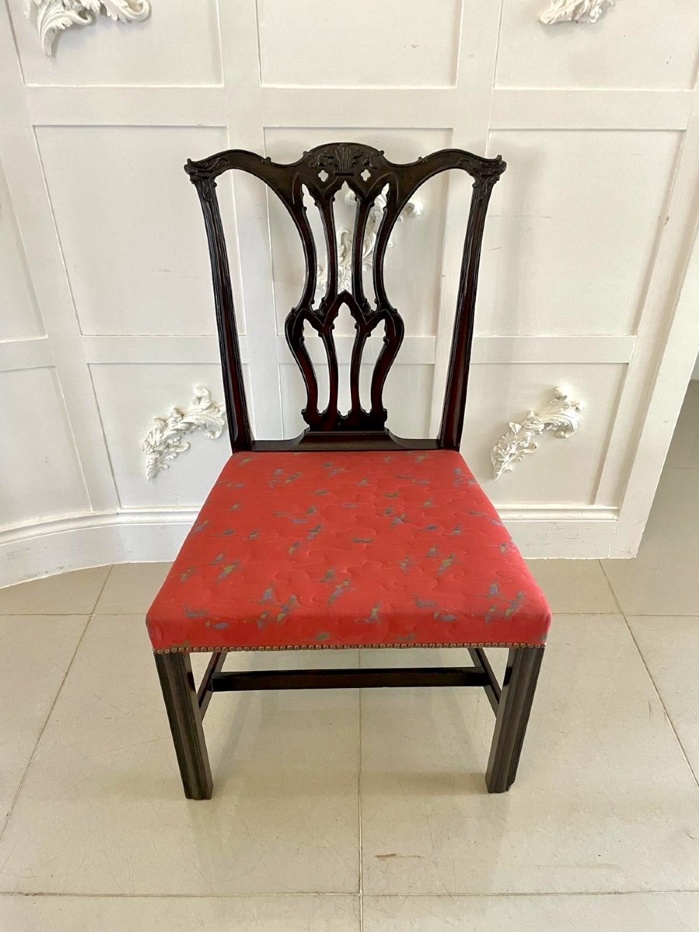 A set of twelve carved dark mahogany dining chairs featuring intricate pierced back splats and red patterned upholstered seats. View VI