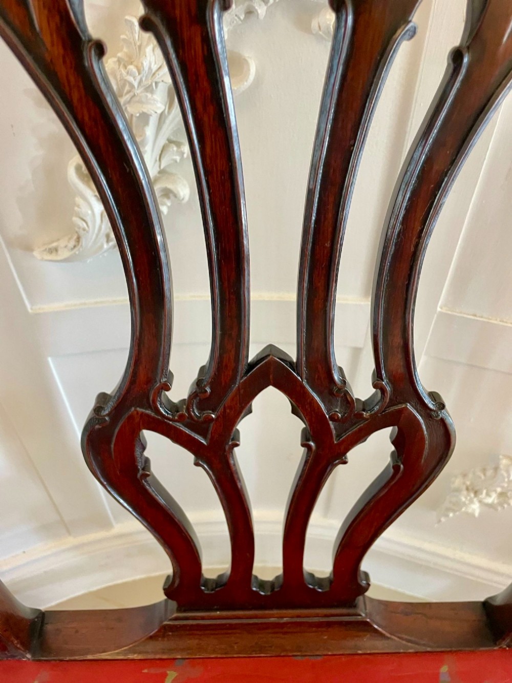 A set of twelve carved dark mahogany dining chairs featuring intricate pierced back splats and red patterned upholstered seats. View X