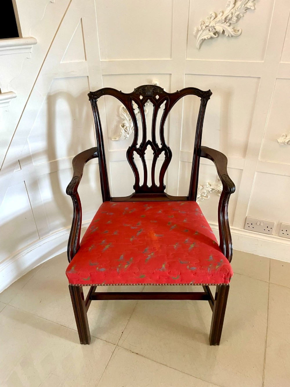 A set of twelve carved dark mahogany dining chairs featuring intricate pierced back splats and red patterned upholstered seats. View XV