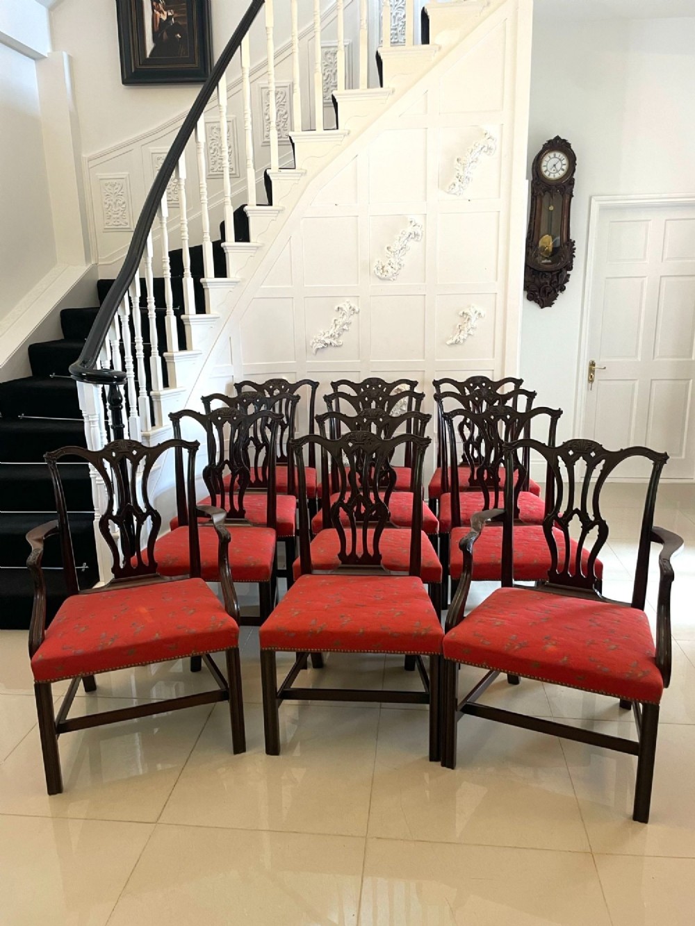 A set of twelve carved dark mahogany dining chairs featuring intricate pierced back splats and red patterned upholstered seats.