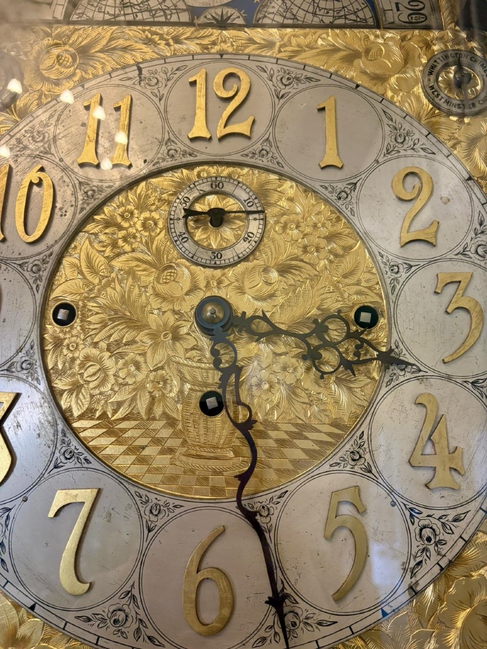 A tall carved dark mahogany longcase clock featuring an ornate pediment, brass dial with moon phase indicator, and a glazed door displaying nine tubular chimes. View V