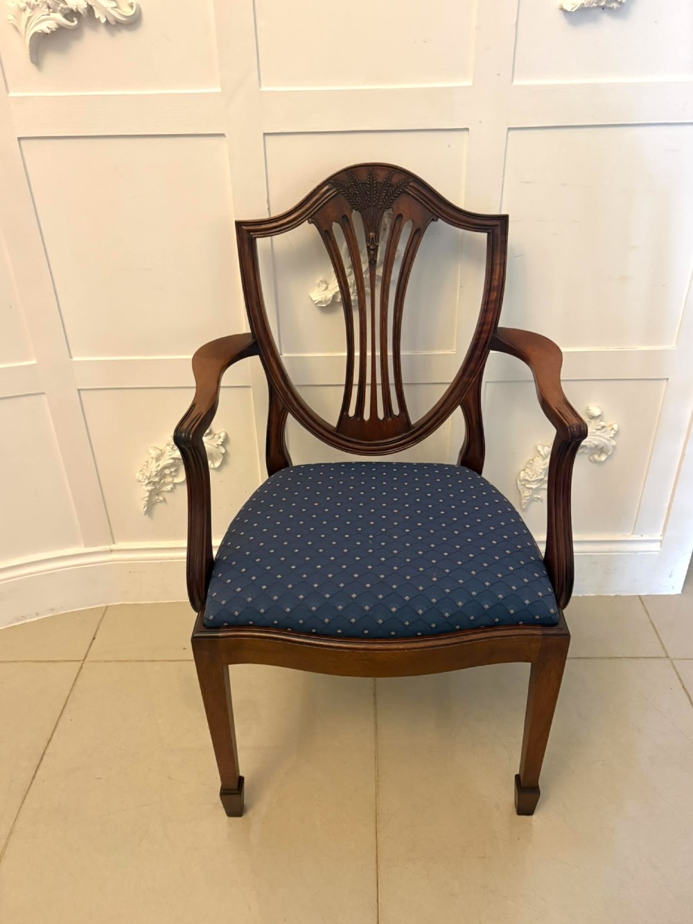 A set of twelve mahogany shield back dining chairs featuring intricate carved splats and patterned blue upholstered seats, arranged in three rows. View IV