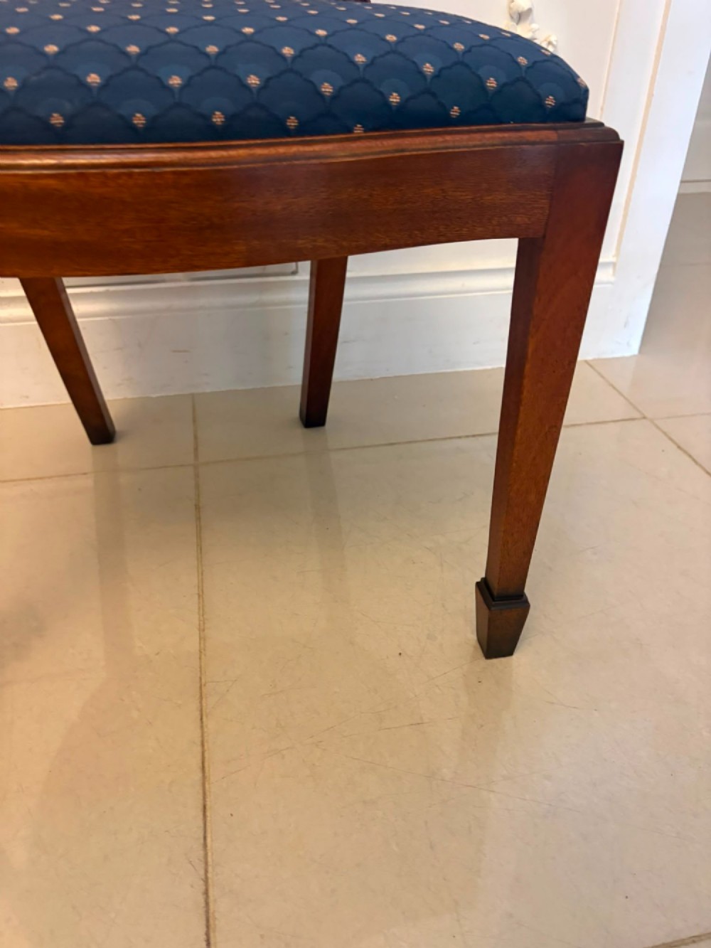 A set of twelve mahogany shield back dining chairs featuring intricate carved splats and patterned blue upholstered seats, arranged in three rows. View XIII