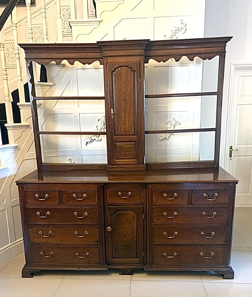 A dark oak Georgian Lancashire dresser with a scalloped open plate rack, central cupboard section, and base containing multiple drawers with brass handles.