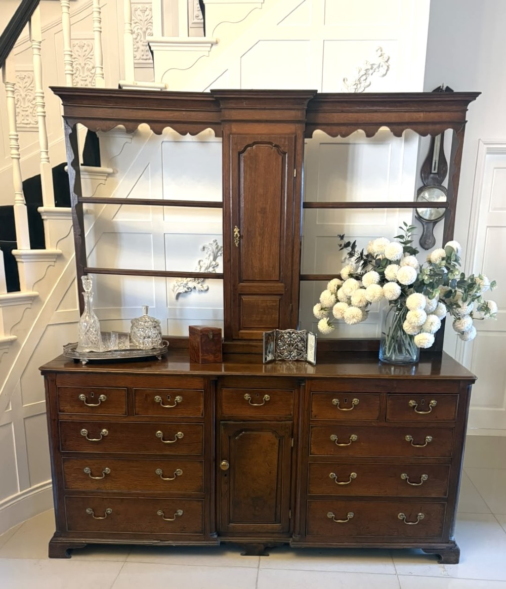 A dark oak Georgian Lancashire dresser with a scalloped open plate rack, central cupboard section, and base containing multiple drawers with brass handles. View VI