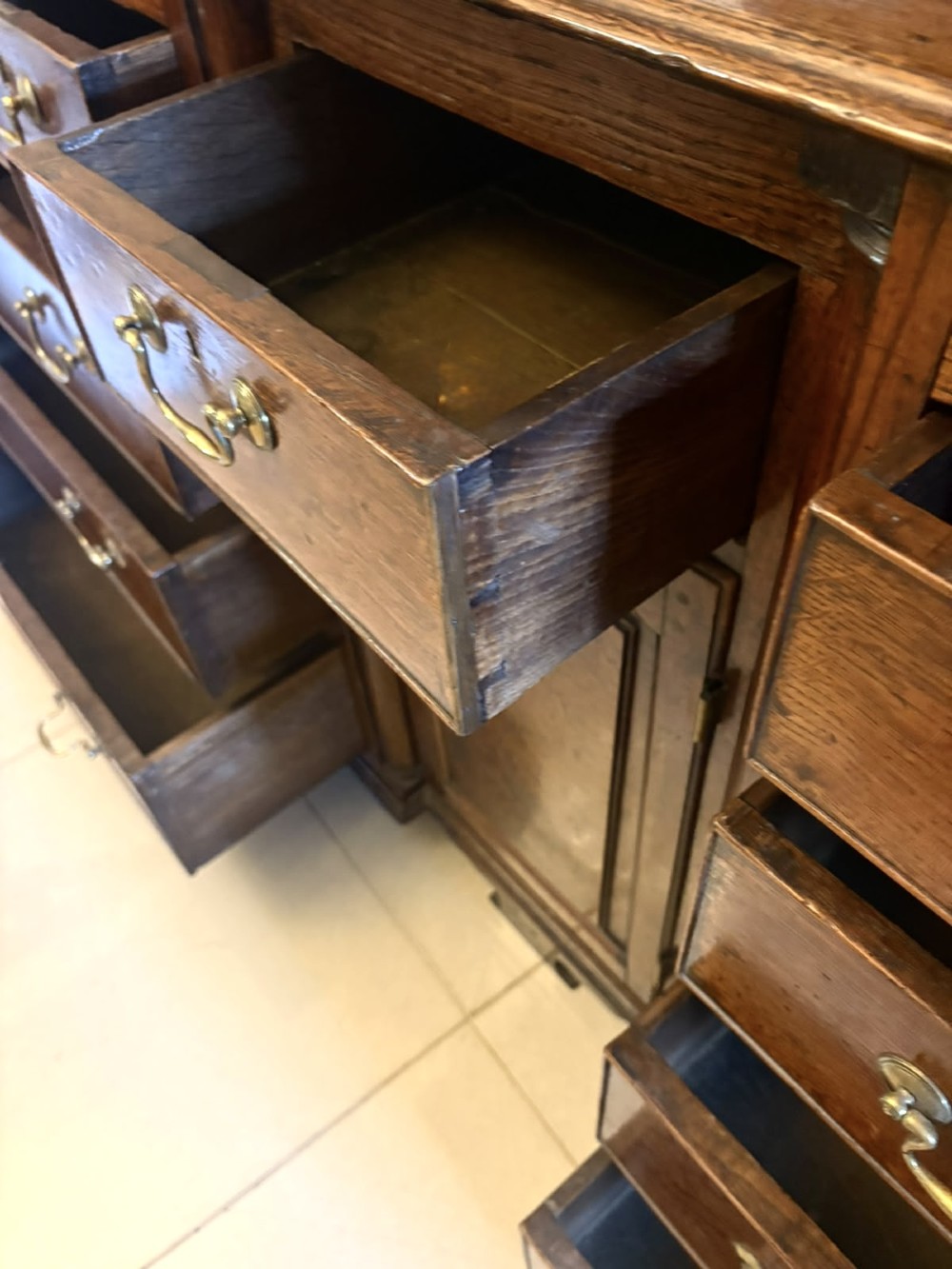 A dark oak Georgian Lancashire dresser with a scalloped open plate rack, central cupboard section, and base containing multiple drawers with brass handles. View VII