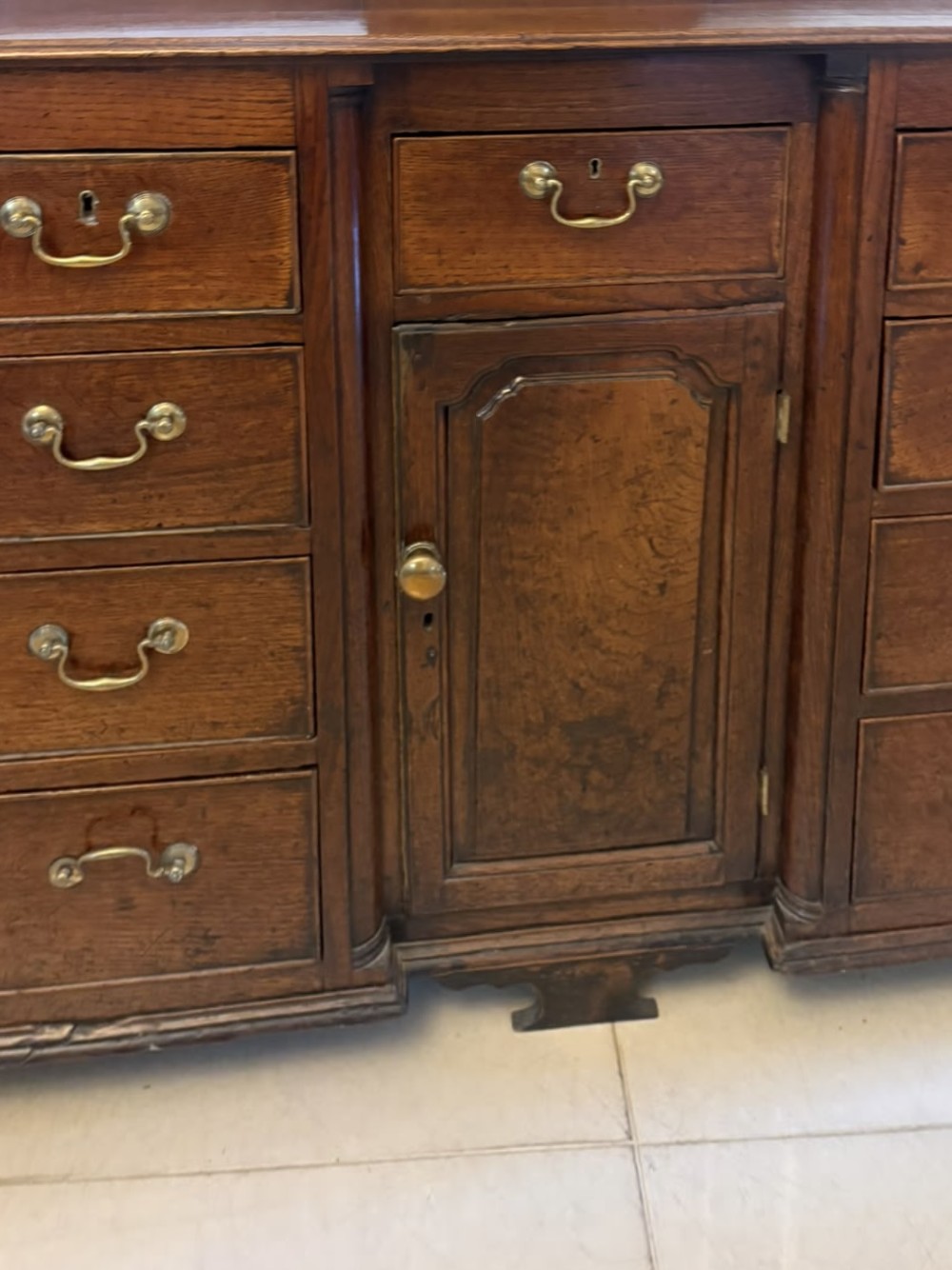 A dark oak Georgian Lancashire dresser with a scalloped open plate rack, central cupboard section, and base containing multiple drawers with brass handles. View X