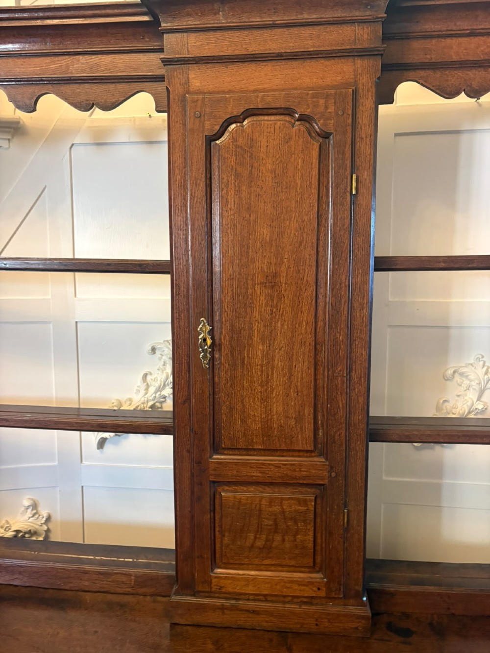 A dark oak Georgian Lancashire dresser with a scalloped open plate rack, central cupboard section, and base containing multiple drawers with brass handles. View XII