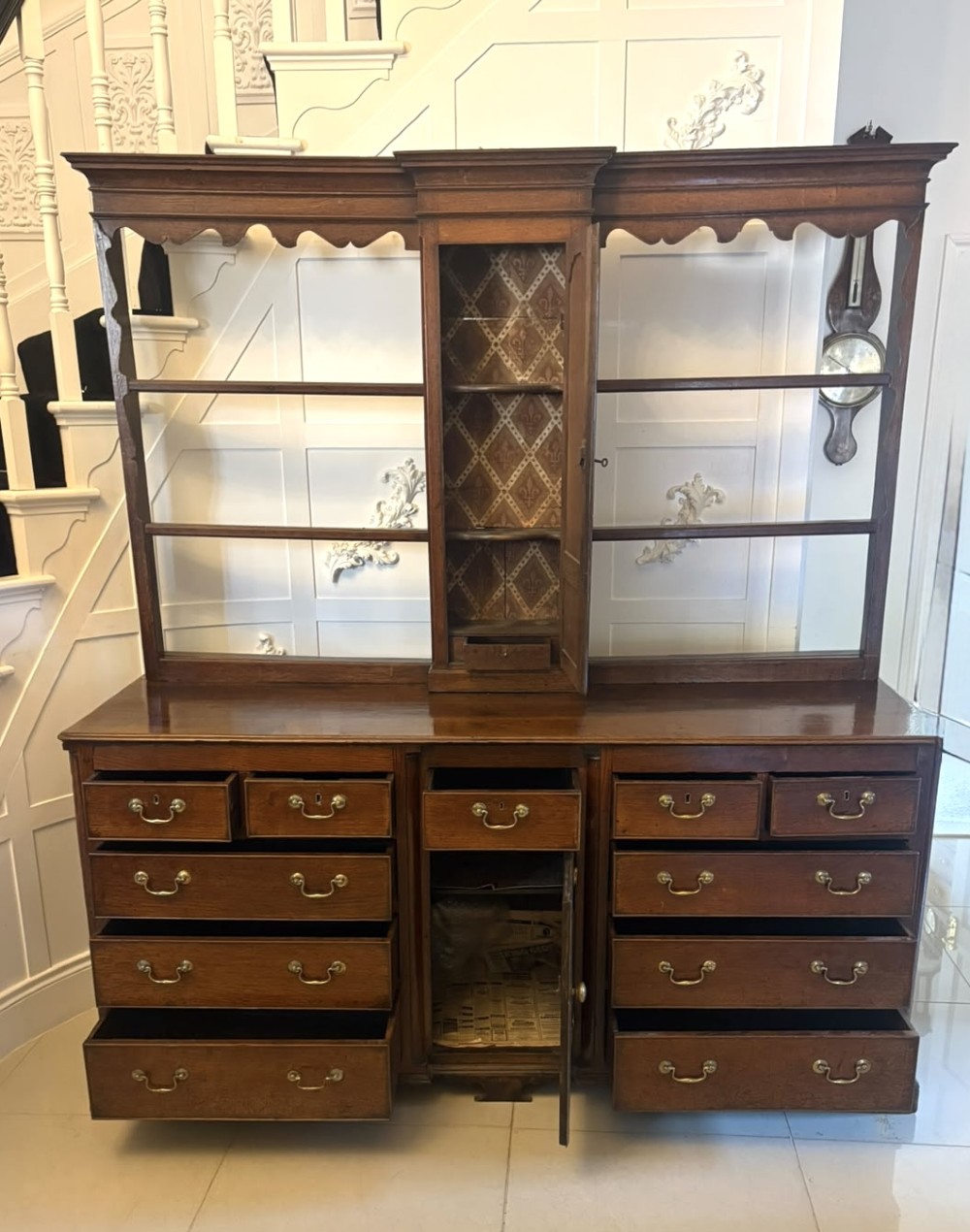 A dark oak Georgian Lancashire dresser with a scalloped open plate rack, central cupboard section, and base containing multiple drawers with brass handles. View XV