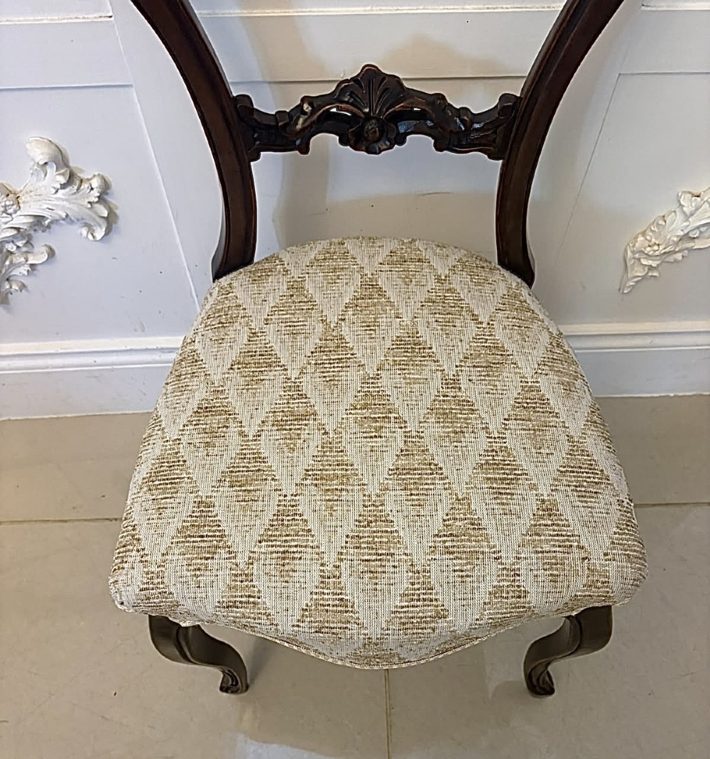 A set of four Victorian carved walnut dining chairs with open balloon-style backs and cream pattern-upholstered seats. View V
