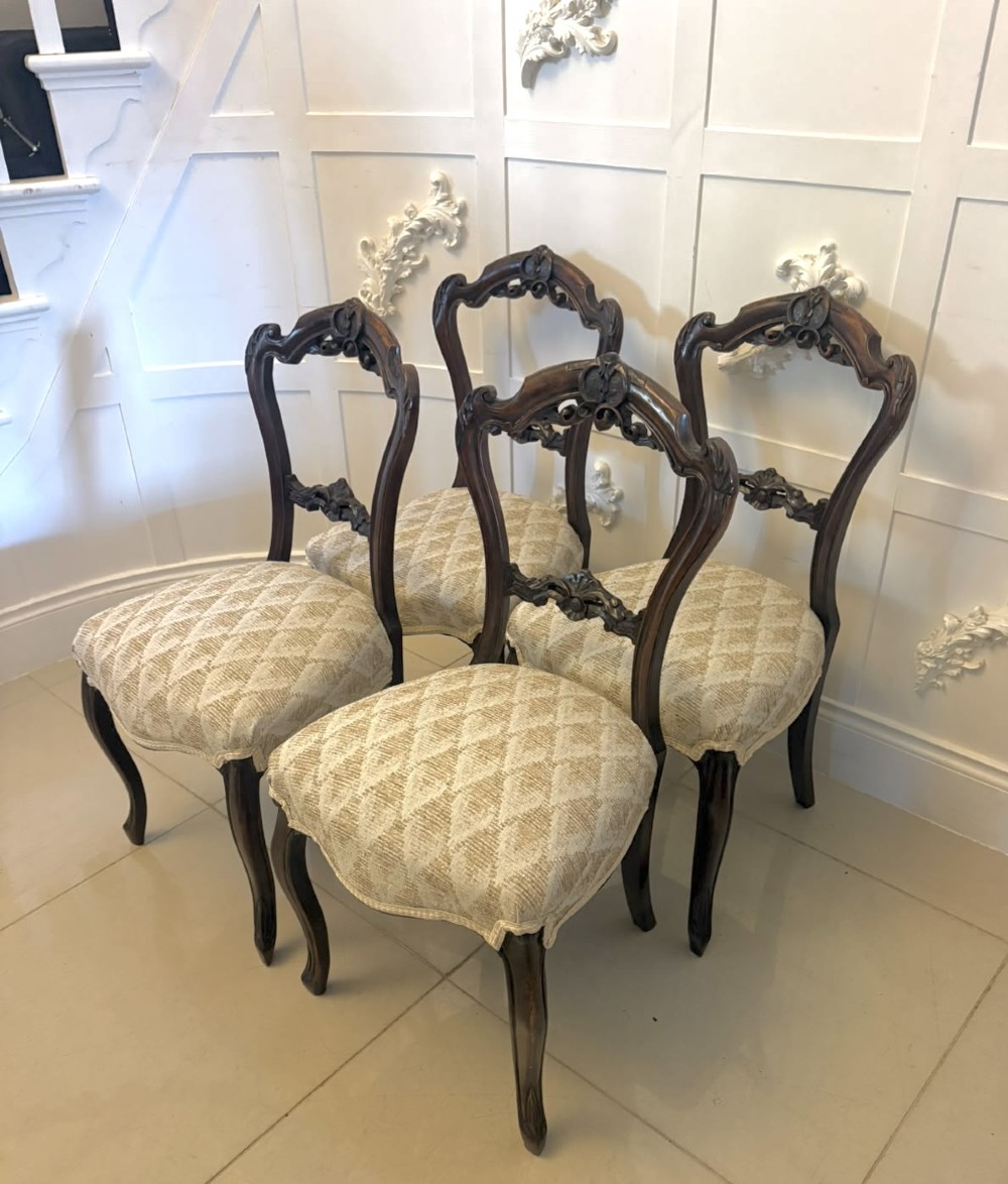 A set of four Victorian carved walnut dining chairs with open balloon-style backs and cream pattern-upholstered seats.
