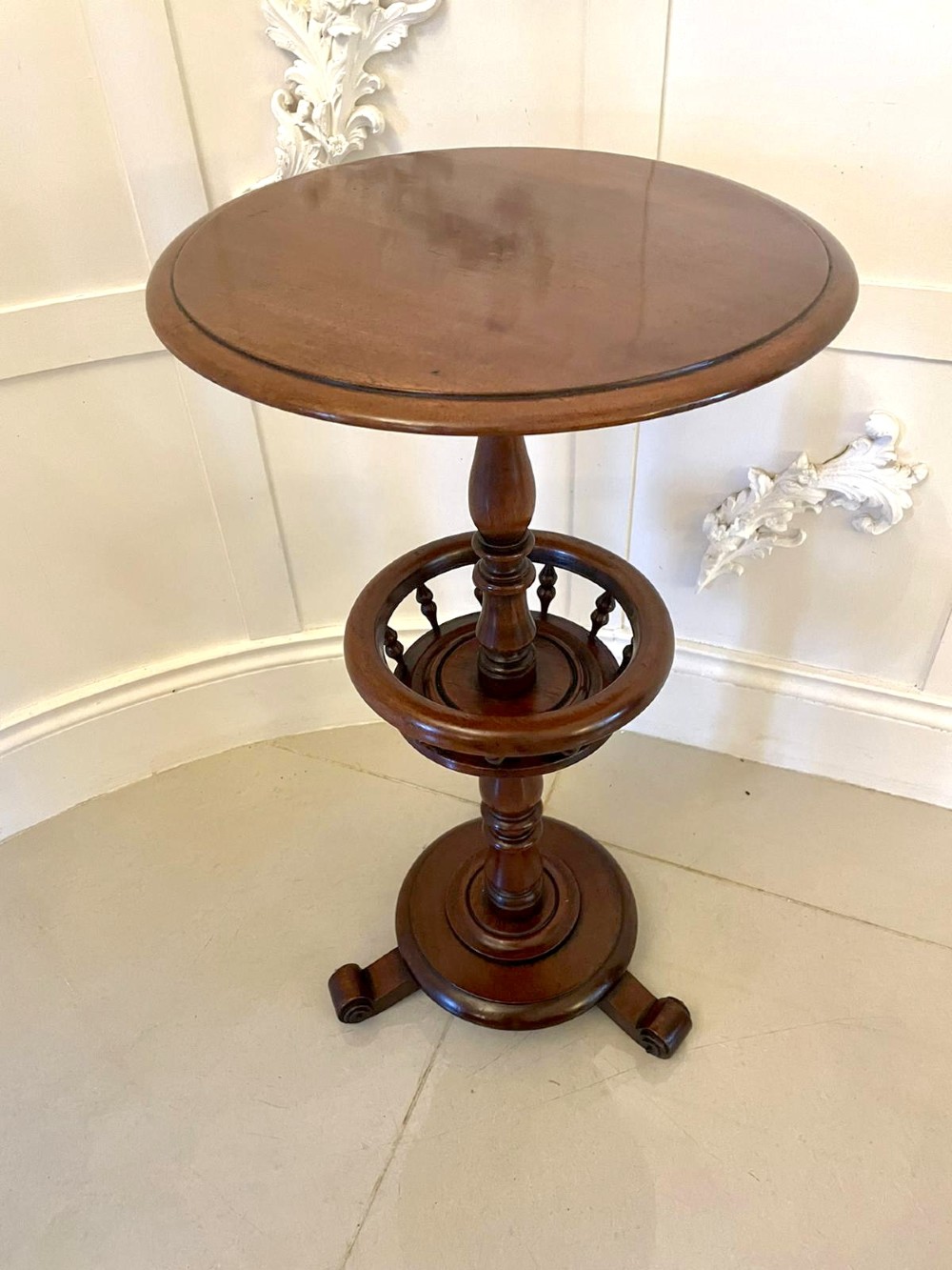 An antique Victorian circular mahogany lamp table featuring a central turned stem with an integrated balustrade mid-tier gallery, resting on a tripod base with scroll feet.