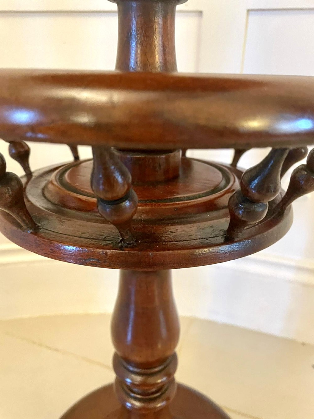An antique Victorian circular mahogany lamp table featuring a central turned stem with an integrated balustrade mid-tier gallery, resting on a tripod base with scroll feet. View X
