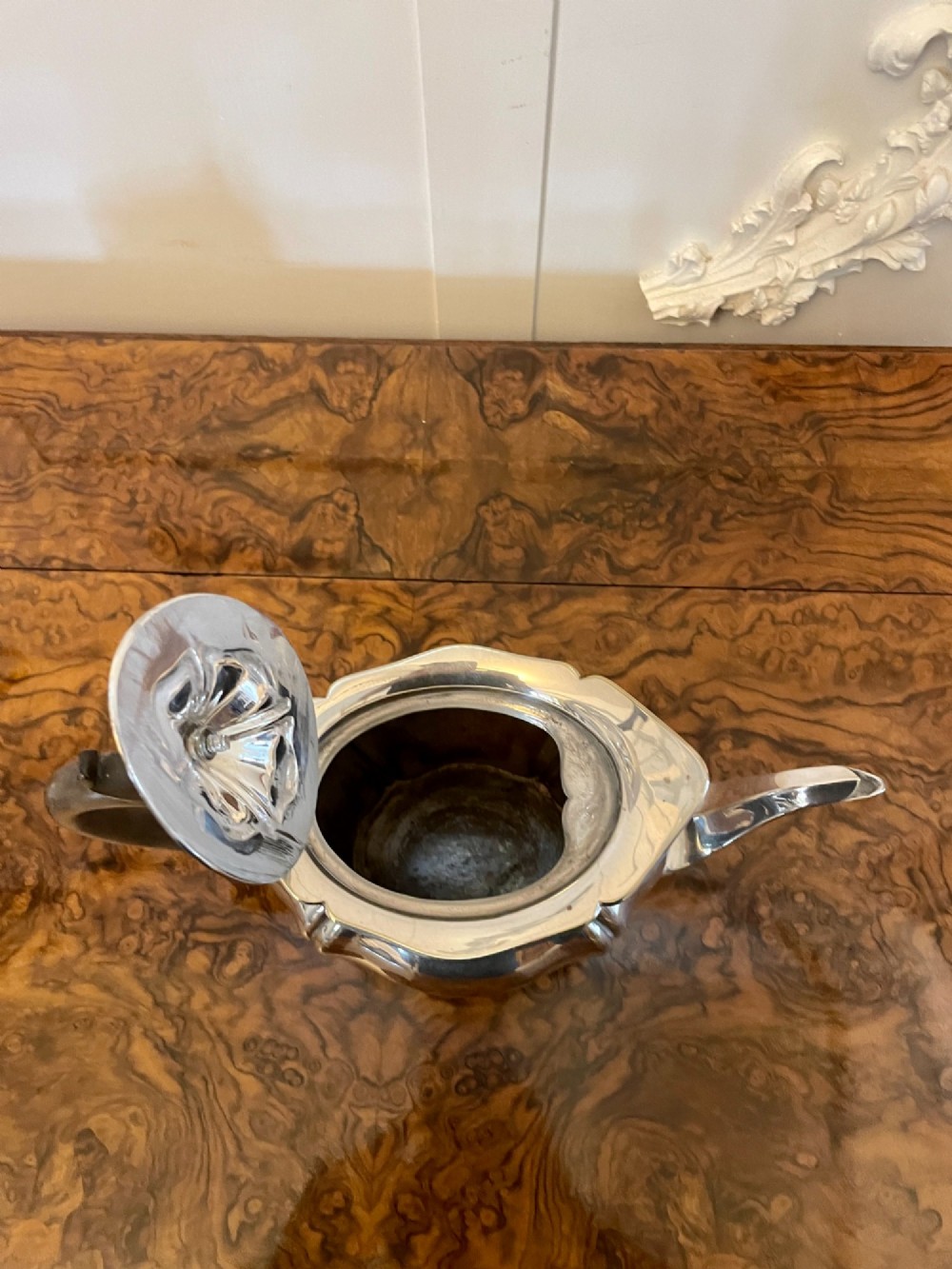 A three-piece Edwardian silver-plated tea set comprising a teapot with a dark wooden handle, a cream jug, and a matching sugar bowl on a polished wood surface. View IV