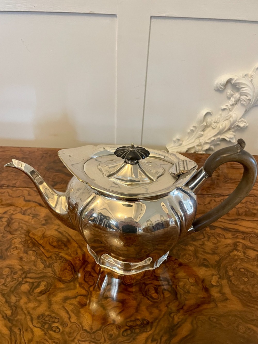 A three-piece Edwardian silver-plated tea set comprising a teapot with a dark wooden handle, a cream jug, and a matching sugar bowl on a polished wood surface. View VII
