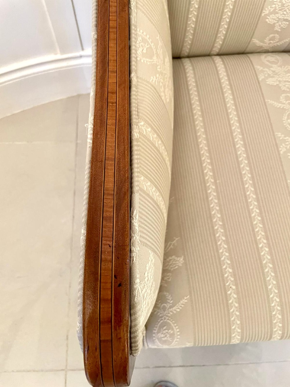 An antique mahogany library armchair upholstered in cream striped fabric, featuring fine timber inlay on the sweeping frame and tapered legs on brass castors. View IX