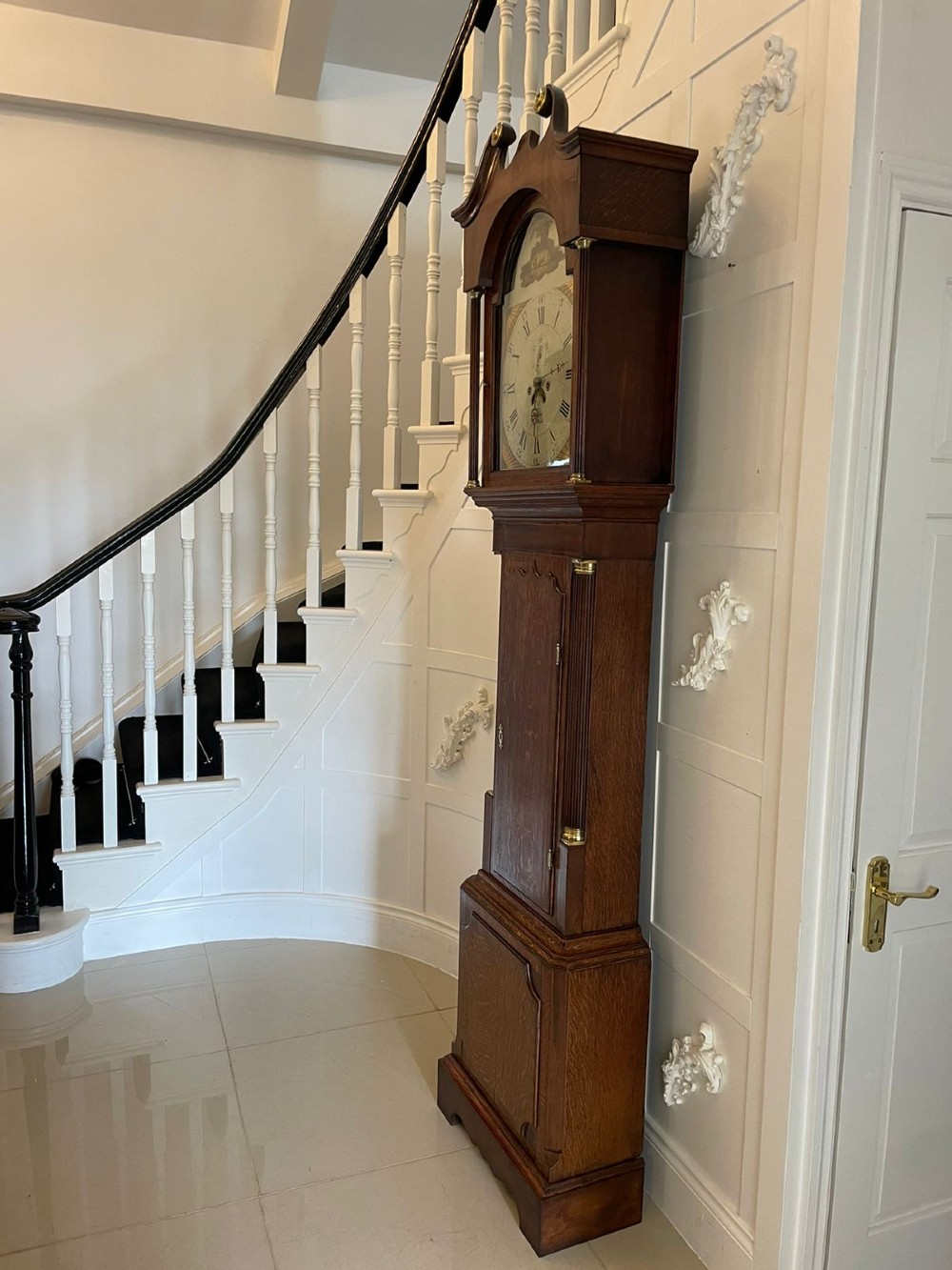 An antique George III oak longcase clock featuring a swan-neck pediment, brass fittings, and a painted arch dial with Roman numerals. View IV