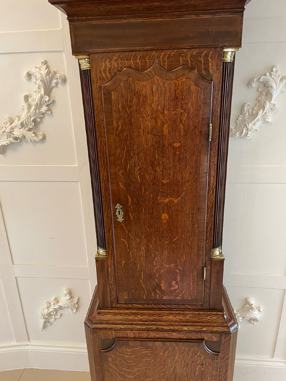 An antique George III oak longcase clock featuring a swan-neck pediment, brass fittings, and a painted arch dial with Roman numerals. View V