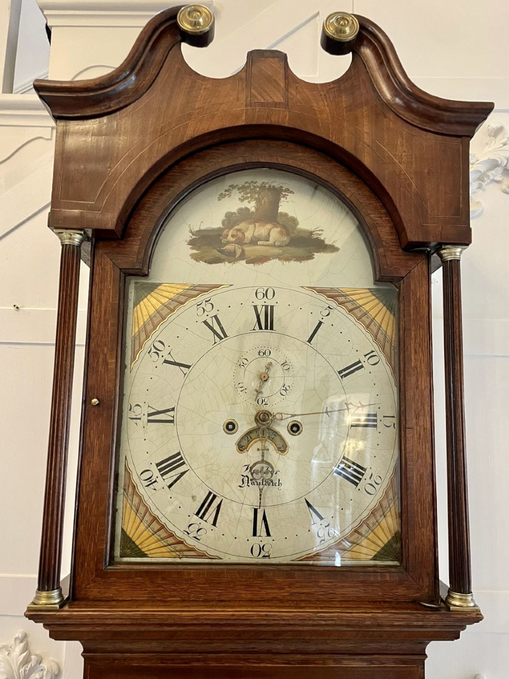 An antique George III oak longcase clock featuring a swan-neck pediment, brass fittings, and a painted arch dial with Roman numerals. View XIV