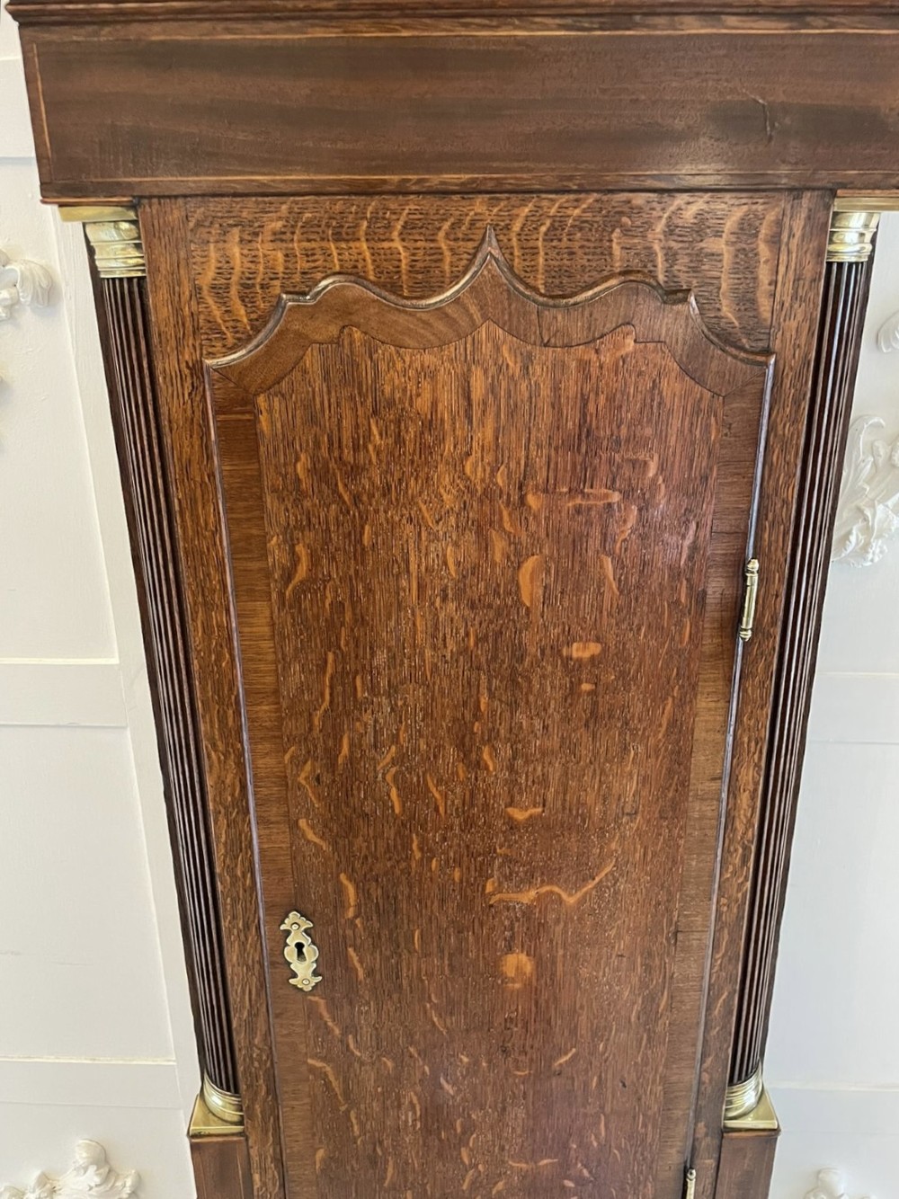 An antique George III oak longcase clock featuring a swan-neck pediment, brass fittings, and a painted arch dial with Roman numerals. View XV