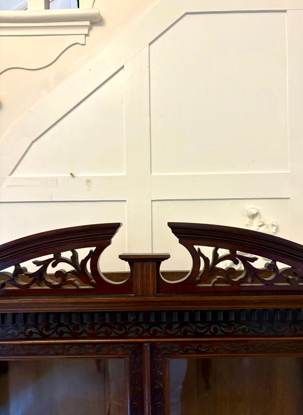A carved mahogany bijouterie display cabinet featuring openwork fretwork pediment, glazed upper doors, and a glass-topped lower display compartment supported by slender legs with an X-shaped stretcher. View VII