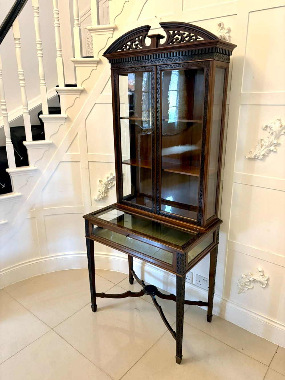 A carved mahogany bijouterie display cabinet featuring openwork fretwork pediment, glazed upper doors, and a glass-topped lower display compartment supported by slender legs with an X-shaped stretcher. View VIII