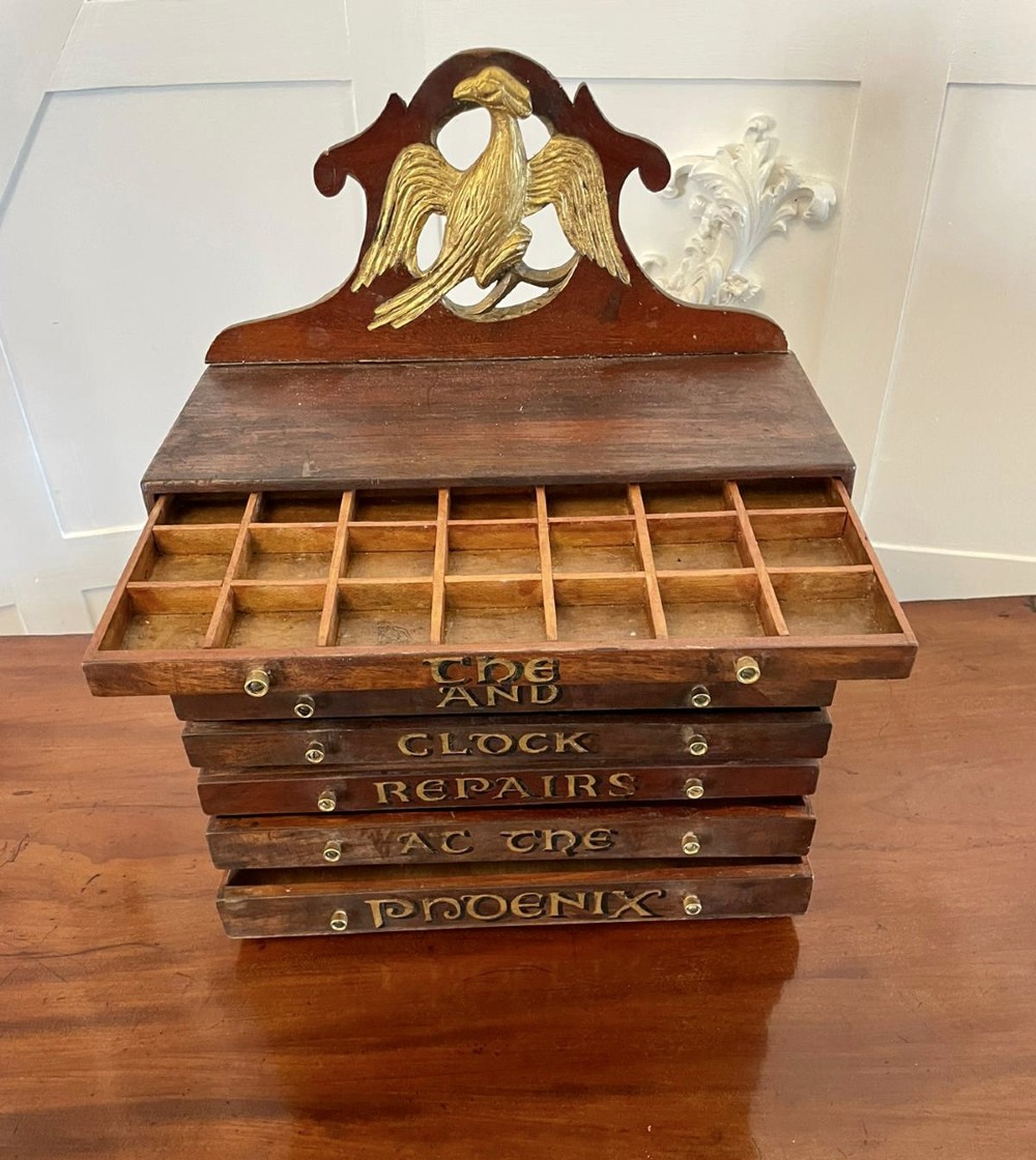 A dark wood Victorian desktop chest of eight shallow drawers featuring carved gilt lettering and a carved phoenix crest on the pediment. View VI
