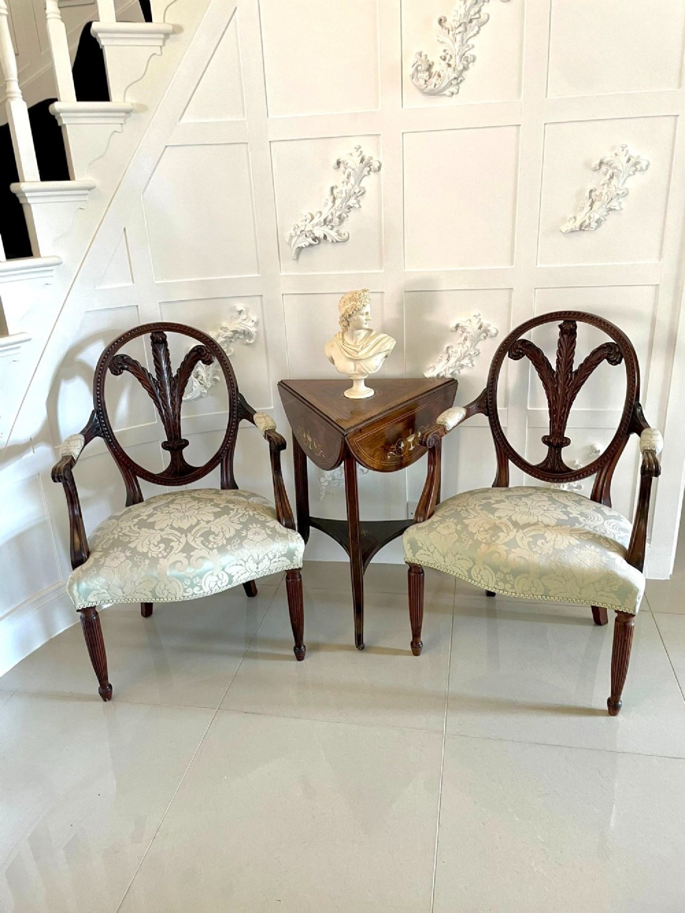 A pair of carved mahogany open armchairs featuring oval backs with carved splats, padded armrests, and pale green patterned fabric seats on fluted front legs. View III
