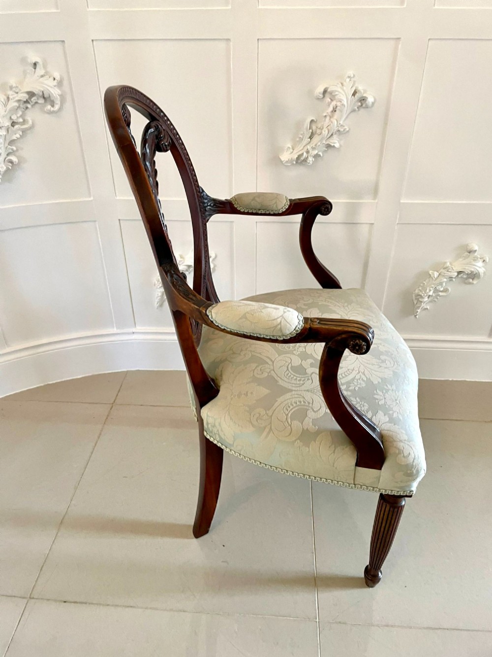 A pair of carved mahogany open armchairs featuring oval backs with carved splats, padded armrests, and pale green patterned fabric seats on fluted front legs. View IV