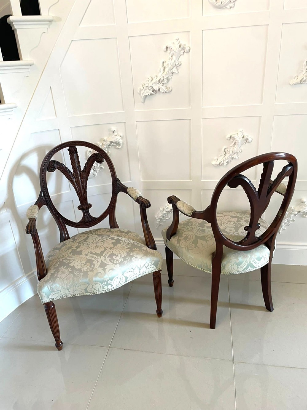 A pair of carved mahogany open armchairs featuring oval backs with carved splats, padded armrests, and pale green patterned fabric seats on fluted front legs. View IX