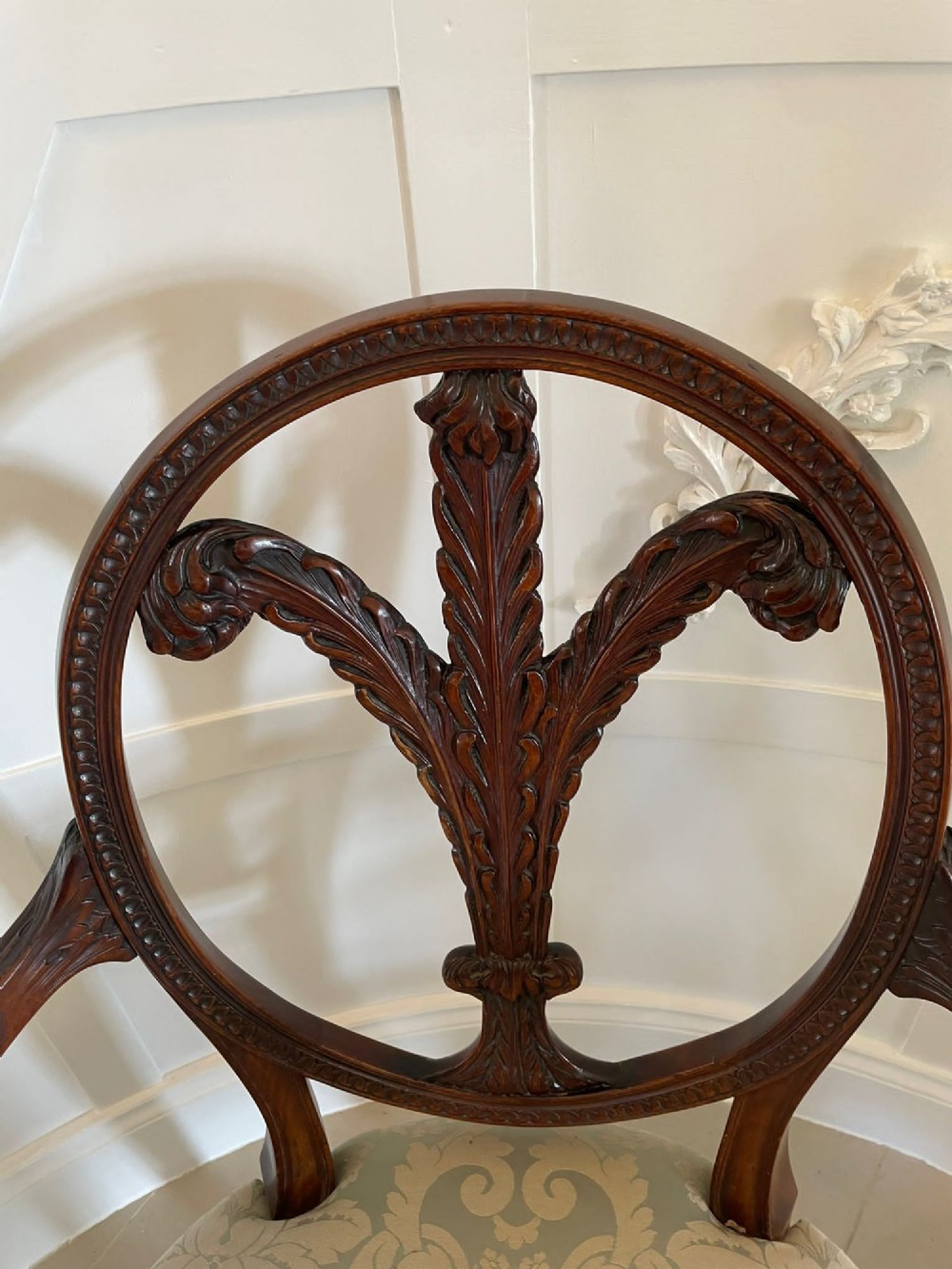 A pair of carved mahogany open armchairs featuring oval backs with carved splats, padded armrests, and pale green patterned fabric seats on fluted front legs. View X