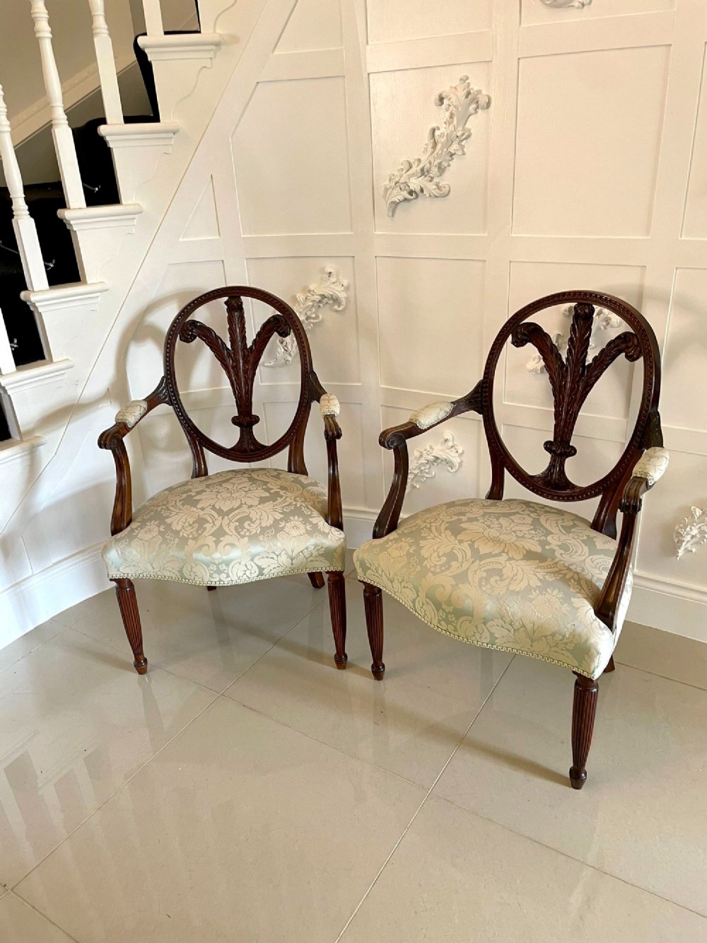 A pair of carved mahogany open armchairs featuring oval backs with carved splats, padded armrests, and pale green patterned fabric seats on fluted front legs. View XII