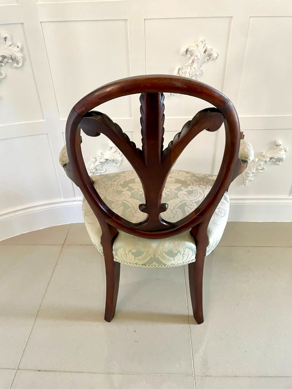 A pair of carved mahogany open armchairs featuring oval backs with carved splats, padded armrests, and pale green patterned fabric seats on fluted front legs. View XV