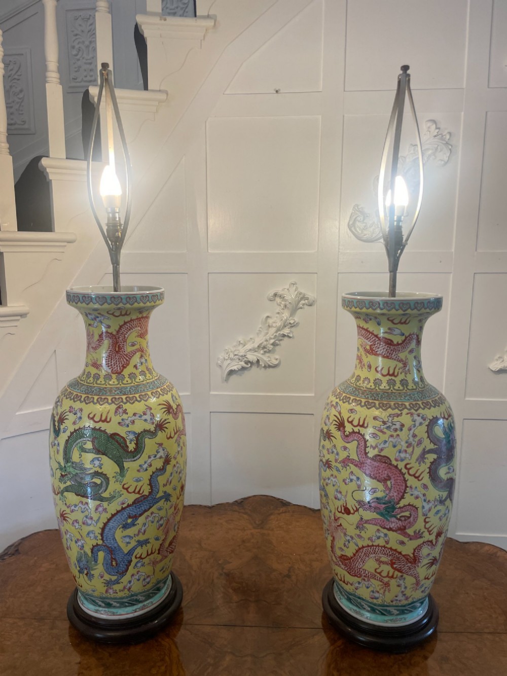 A pair of large 19th-century Chinese porcelain vase lamps featuring hand-painted dragons on a yellow ground, set on dark wooden bases.
